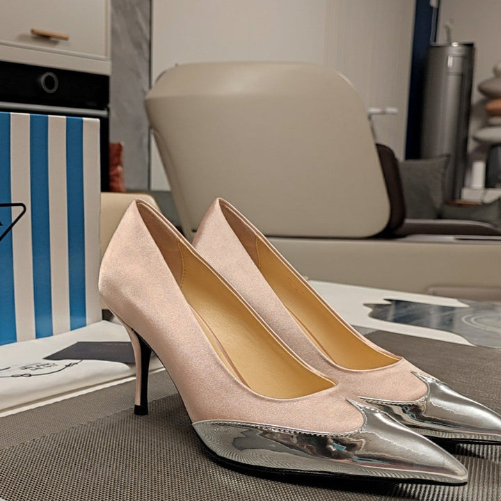 Pair of beige high-heeled shoes with silver tips on a table next to a Prada box.