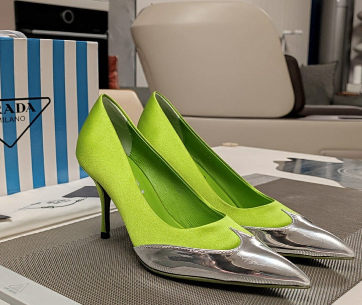 Green high-heeled shoes with silver toes on a table in front of a Prada box.